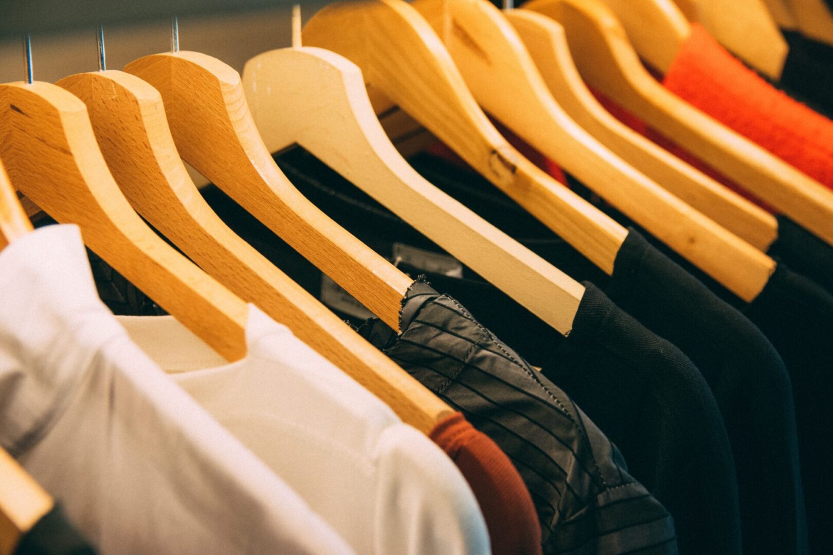 Assorted clothing items hung on wooden hangers in a store.