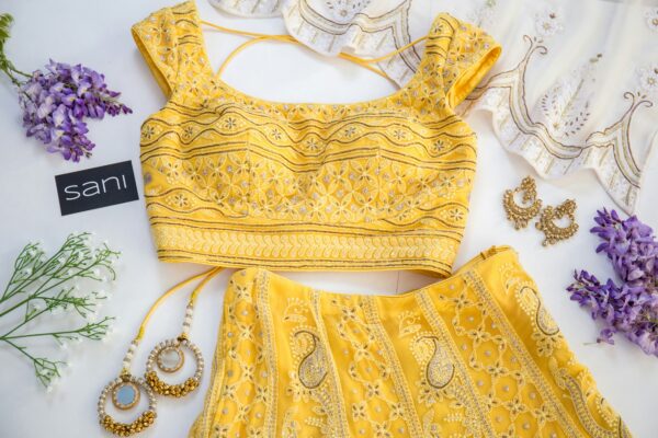 Yellow embroidered traditional indian blouse with accessories and flowers on a white background.